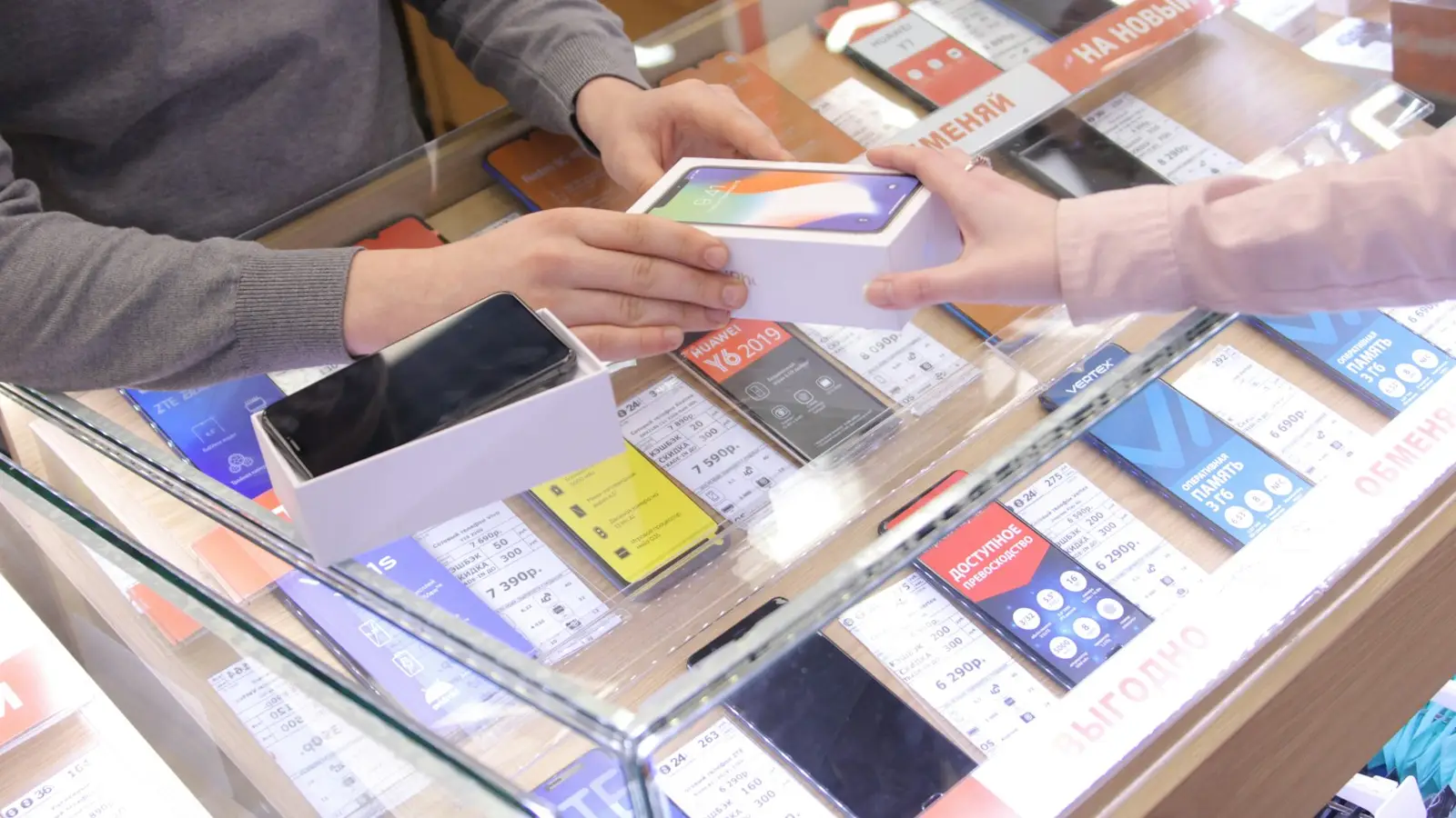 A smartphone being handed across a glass shop counter