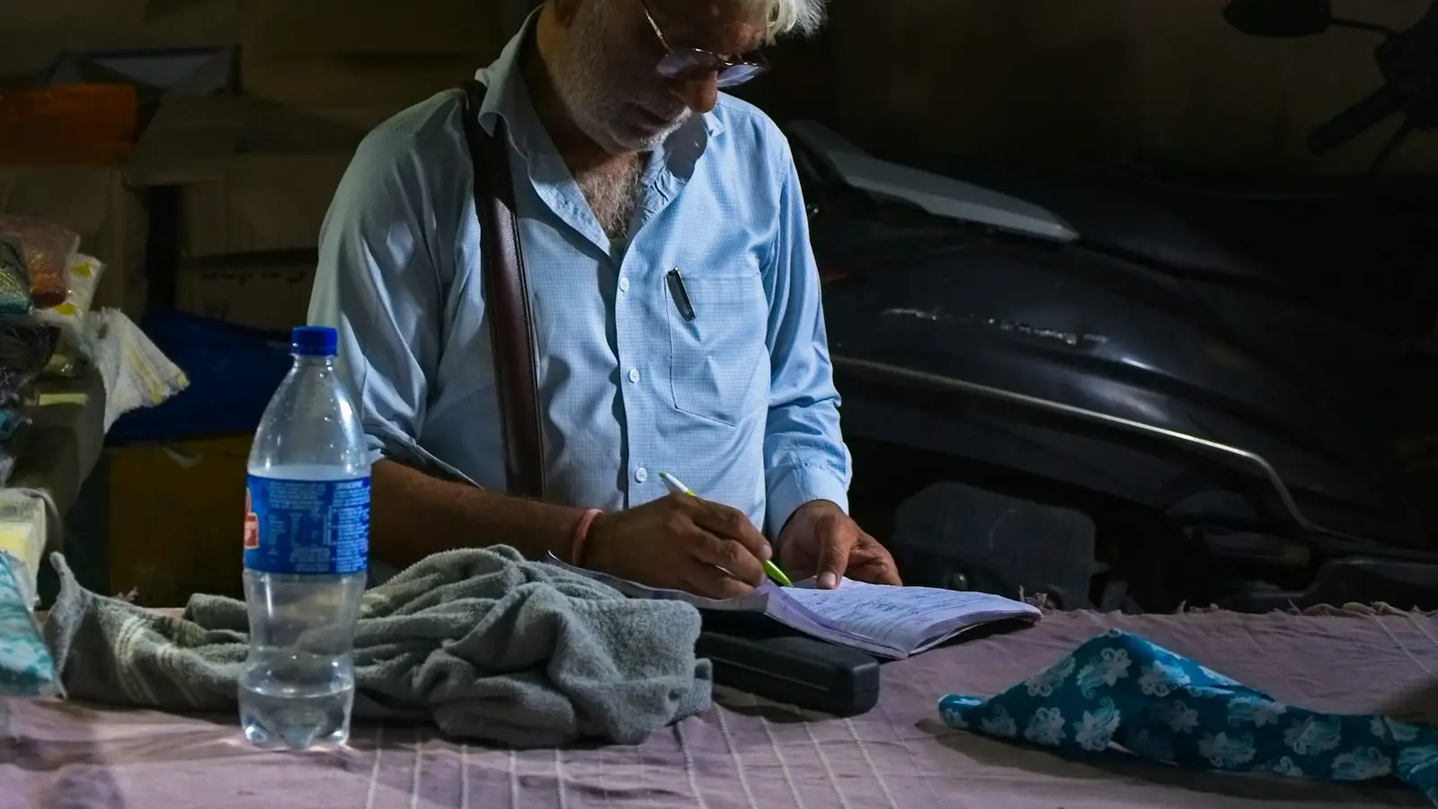 An elderly man writing in a notebook at his desk